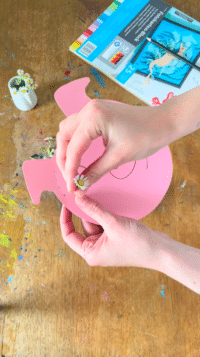 Hand steckt Blumen in die Löcher des gebastelten Schweinkopfs