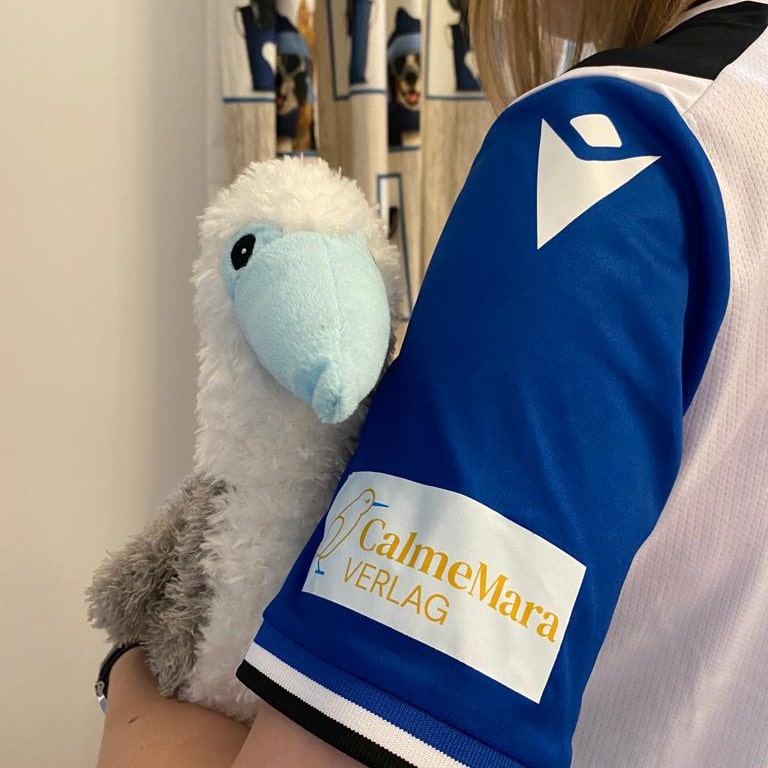 Plüschtier Bo Blaufuß wird von einer Person mit CaleMara-Ärmel gehalten