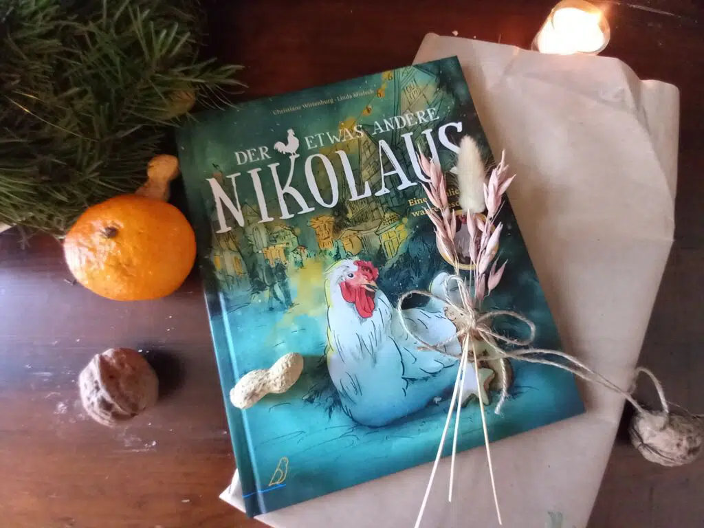 das Buch "Der etwas andere Nikolaus" mit zusammengeknoteten Blumen, Nüssen, einer Kerze, einer Orange und Geschenkpapier daneben