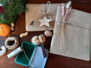 zwei Geschenke mit naturbraunem Geschenkpapier, daneben liegen Nüsse, eine Orange, Faden und eine Schatulle