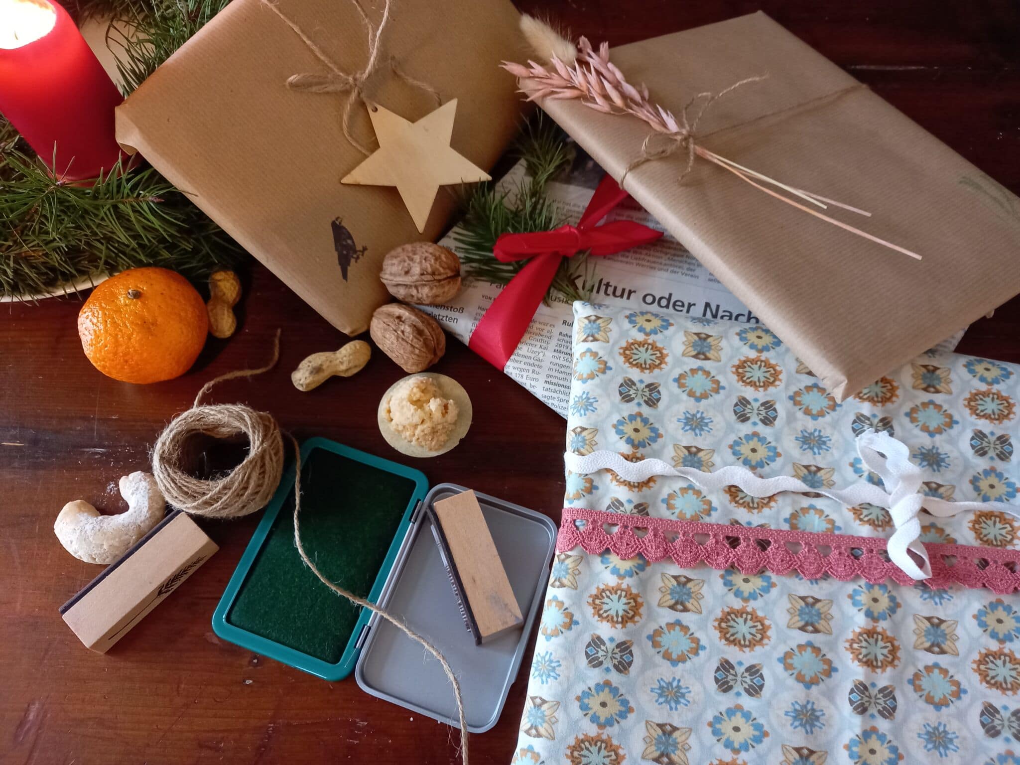 drei Geschenke Geschenkpapier, daneben liegen Nüsse, eine Orange, Faden und eine Schatulle