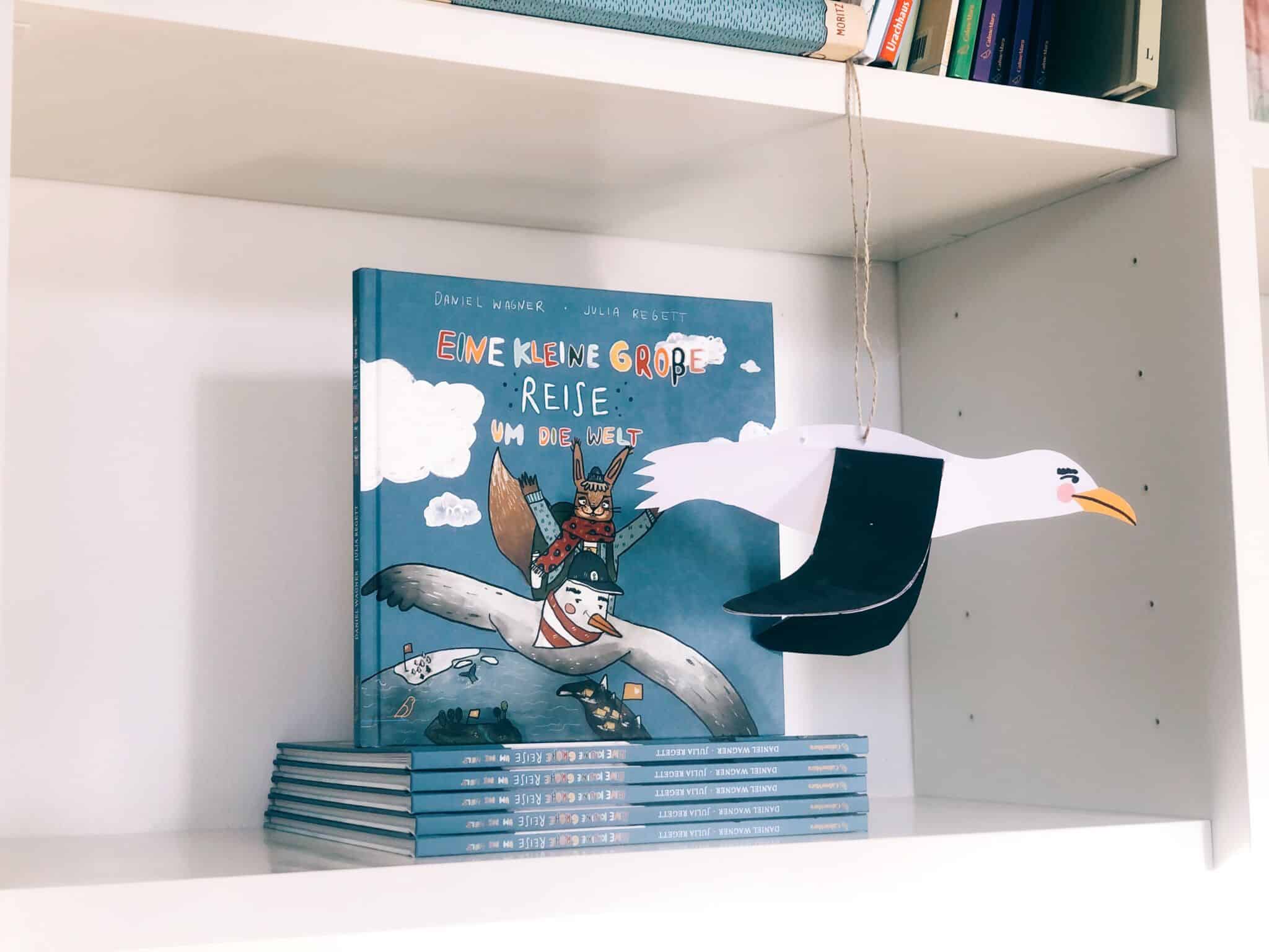 gebastelter Albatros Arthur hängt an einem Faden vor einem Regal mit dem Buch " Eine kleine große Reise "