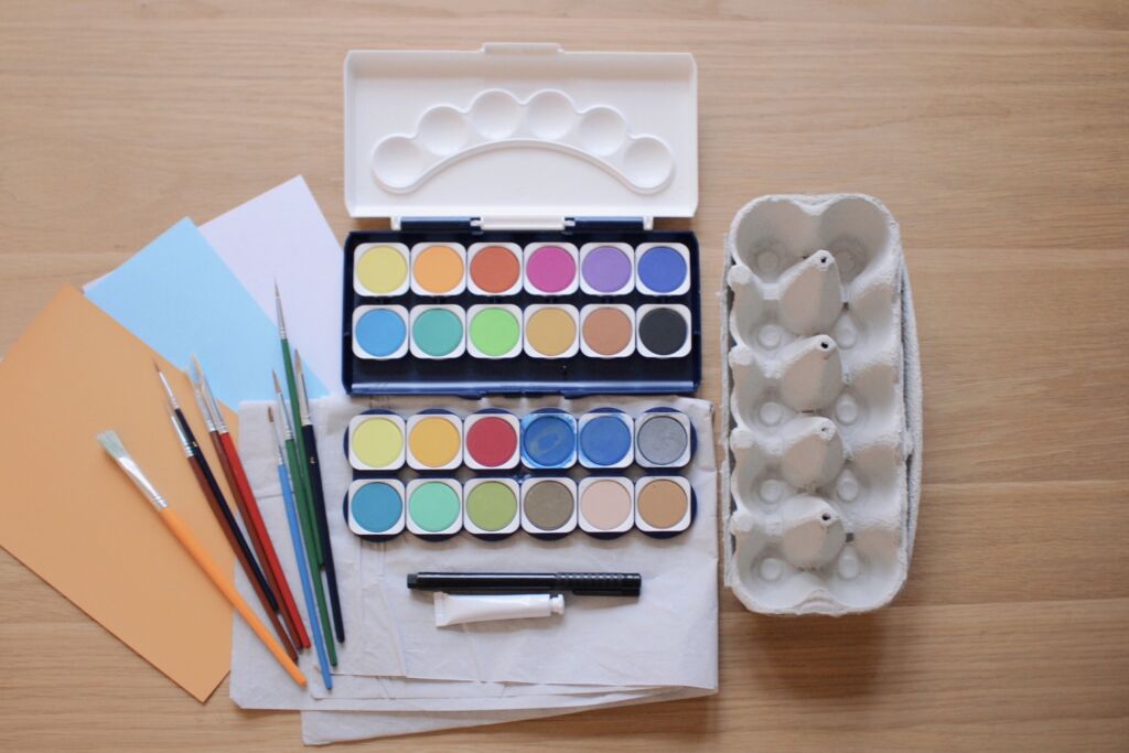ein Farbkasten, mehrere Pinsel, Deckweiß, Papier und ein Eierkarton