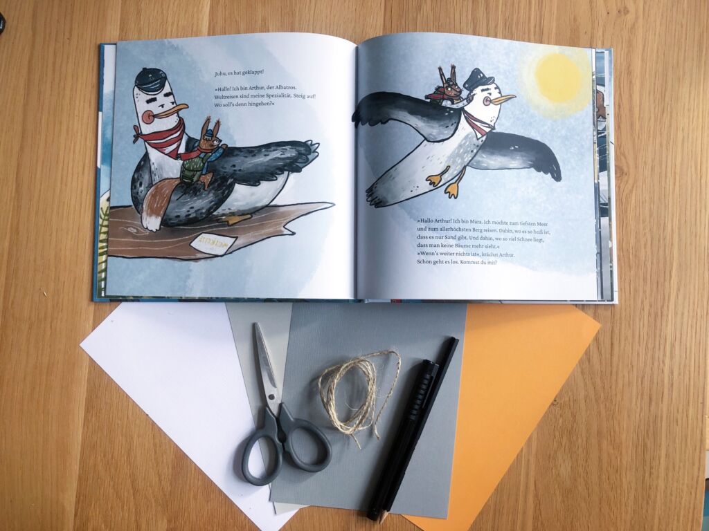 aufgeschlagenes Buch "Eine kleine große Reise"; daneben liegen Papier, eine Schere, ein Faden und Stifte