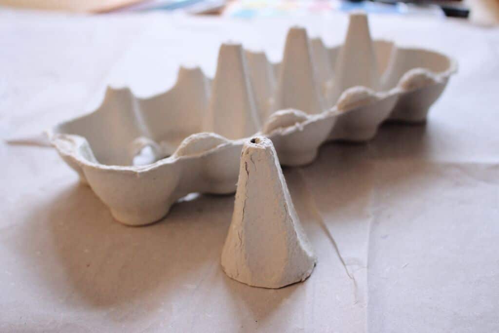 ein Eierkarton, dem ein kegelförmiges Stück Pappe herausgeschnitten wurde, das neben dem Karton steht