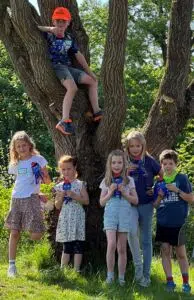 mehrere Kinder mit Oktopus-Plüschtier neben einem Baum, ein Kind auf dem Baum