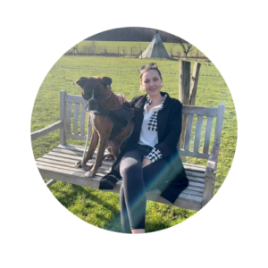 Frau mit Hund sitzt auf einer Parkbank vor einer grünen Wiese