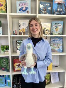 Jasmin_klein EIne Frau mit kurzen Blonden Haaren und blauer Bluse hält unseren Verlagsvogel Bo im Arm.