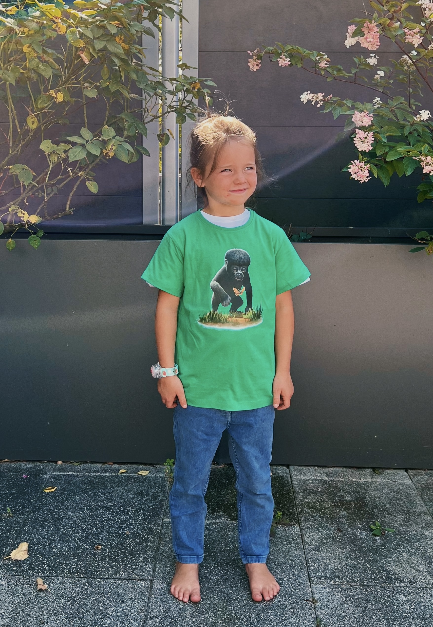 Ein Kind steht im Garten und trägt ein grünes T-Shirt mit Gorilla-Aufdruck