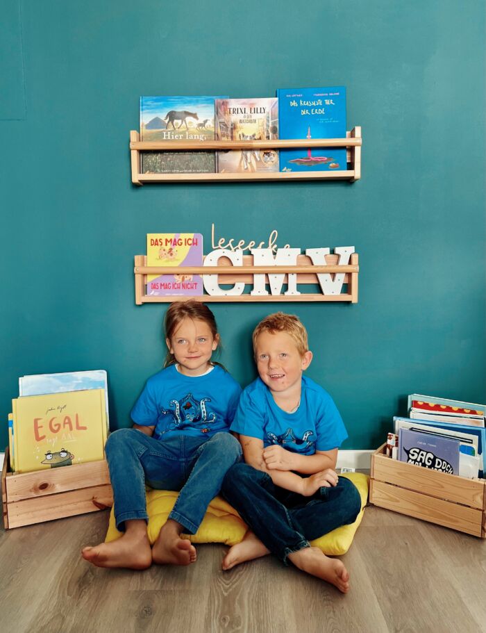 Zwei Kinder sitzen in einer Leseecke und tragen blaue T-Shirts mit Oktopus-Aufdruck